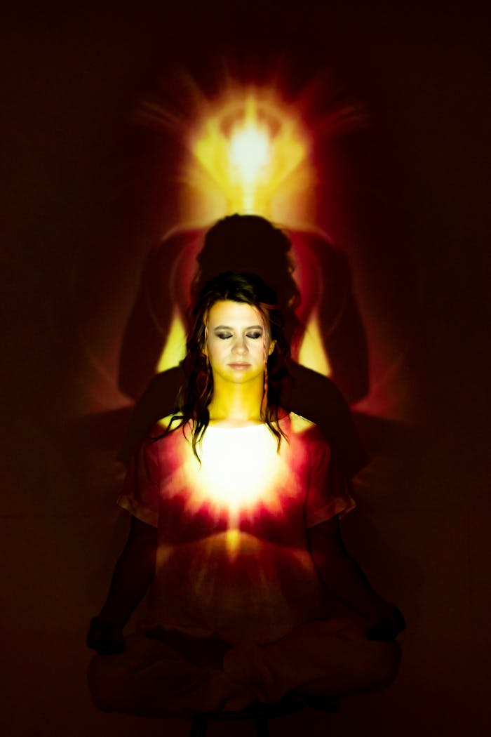 A woman sits in a lotus position with eyes closed, enveloped in a vibrant aura, symbolizing inner peace.